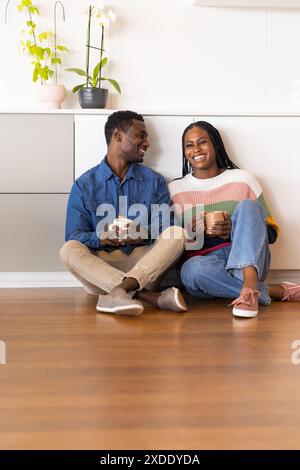 Young couple sitting on floor, holding coffee cups and smiling at each other Stock Photo