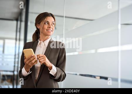 Happy busy middle aged woman business owner looking away using mobile phone. Stock Photo