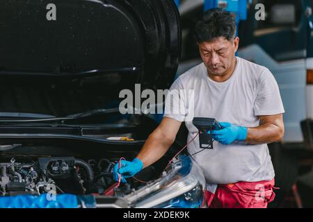 Worker checking Car Battery Voltage with Multi meter, Technician metering vehicle electricity at front hood. Stock Photo