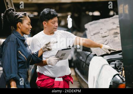 Mature expert mechanic man training young teen women worker to check service car using tablet technology. Stock Photo