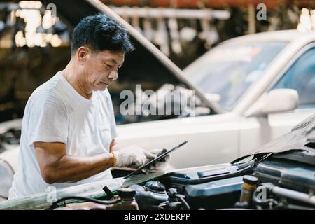 Garage Asian professional working auto service checking engine. Mechanic man using tablet computer tuning car ECU. Stock Photo
