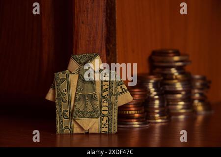 A shirt made from a dollar bill and a stack of coins stand on a wooden cabinet, business and finance, dollar Stock Photo