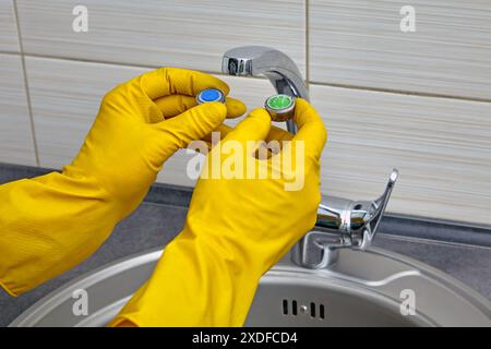 Plumber's hands in yellow rubber gloves change an old clogged kitchen sink faucet aerator to a new one Stock Photo