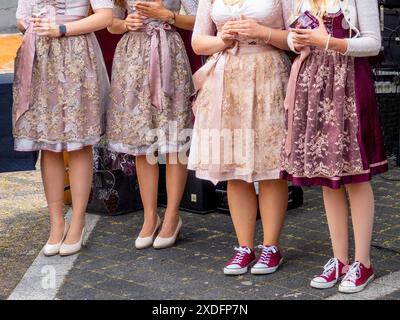 Four women wearing traditional dirndl dresses stand in a group outdoors. They are wearing different colored dirndls and have chosen to wear casual sho Stock Photo