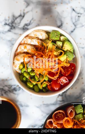 A poke bowl of food with a variety of vegetables including carrots, tomatoes, avocado and edamames and shrimps. The bowl is on a marble background Stock Photo