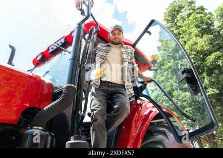 Low angle view portrait of male farm tractor driver on a red tractor in summer. Stock Photo