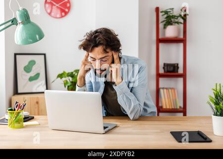 Exhausted man suffering from headache while working on his laptop. Stock Photo