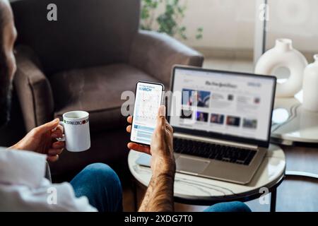 Man looking at calendar on mobile phone early in the morning for planning the day. News site on the laptop screen. Digital schedule concept. Stock Photo
