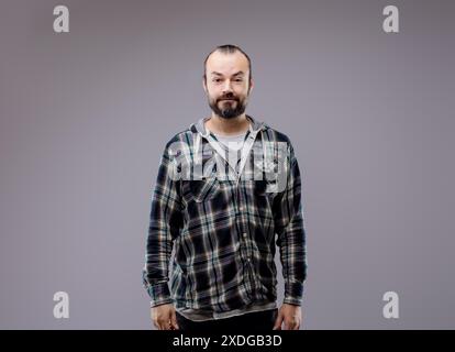 Confident man in plaid shirt standing against grey background, conveying seriousness and thoughtfulness. Shows healthy lifestyle and casual style Stock Photo