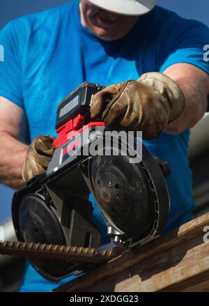 Large, unidentifiable man in blue shirt, uses a cordless band saw to cut through a piece of rebar. Construction yard, daytime. Stock Photo