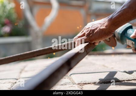 Close-up of a person using an angle grinder to cut a metal rod, with sparks flying. The background is blurred, focusing on the hands and the tool. Stock Photo