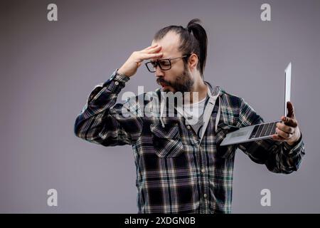 Technician is holding a laptop and regretting checking it because it has a security problem. He is feeling disappointed about what he saw Stock Photo