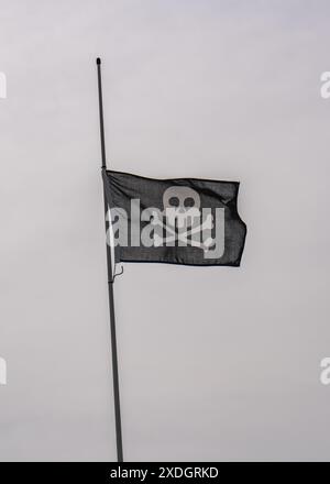 A generic pirate flag flutters in the wind against the sky.Skull and bones Stock Photo