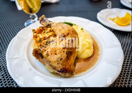 Baked chicken leg with pastry stuffing on mashed potato on white plate on restaurant table. Stock Photo