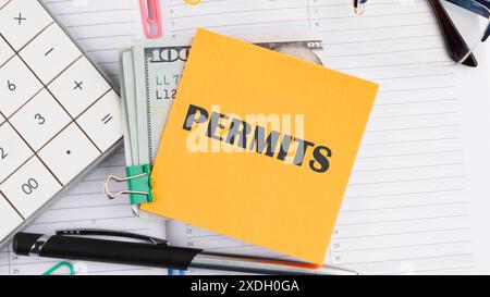 Business concept, Permit word written on a yellow sticker next to American hundred dollar bills, a calculator, a pen on a white background Stock Photo