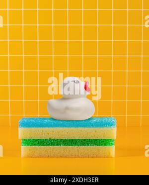 Fashionable white duck with red beak on multicolored sponges, yellow tiles backdrop Stock Photo