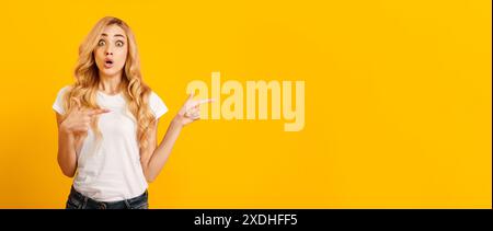 Surprised Woman Pointing to Side on Yellow Background Stock Photo