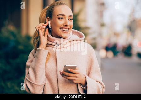Happy Woman Using Smartphone and Earbuds in Urban Setting Stock Photo