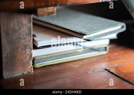 A close-up of a stack of notebooks and journals placed on a wooden shelf. The notebooks have different covers and are stacked neatly. Stock Photo