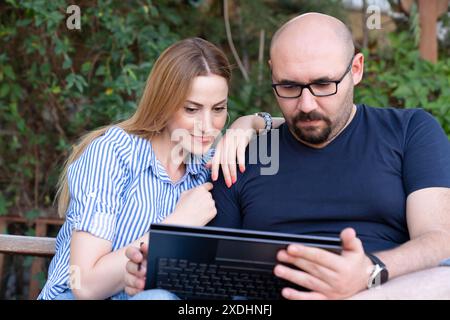 Happy young multiethnic couple spending time together at the park, studying while with laptop Stock Photo
