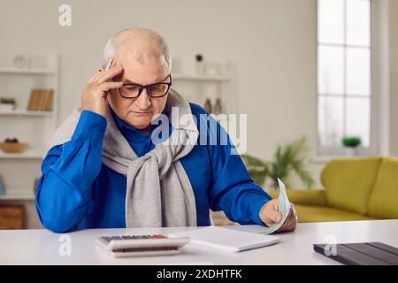 Focused senior man using calculator and laptop sitting at desk Stock Photo