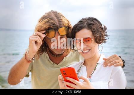 Smiling couple on the beach browsing smartphone apps. Stock Photo