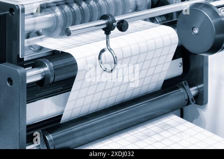 A roll of white paper is passed through the machine. printer and sticker machine, which is used for printing and applying stickers to packaging indust Stock Photo