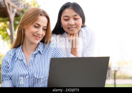 Happy young multiethnic couple spending time together at the park, studying while sitting at the table with laptop Stock Photo