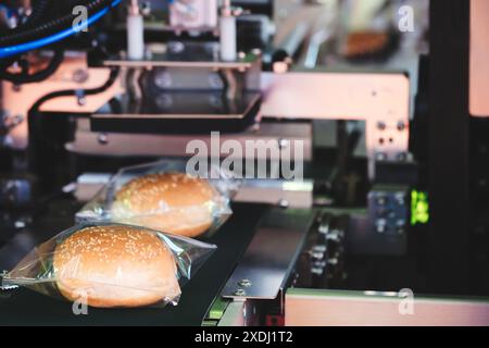 A machine is making hot dogs in plastic bags. The bags are being placed on a conveyor belt Stock Photo