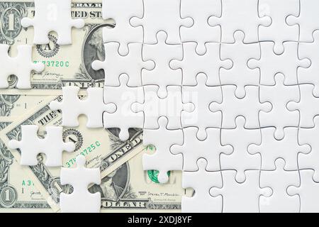 A white jigsaw puzzle with a missing piece revealing an image of a banknote in the background Stock Photo