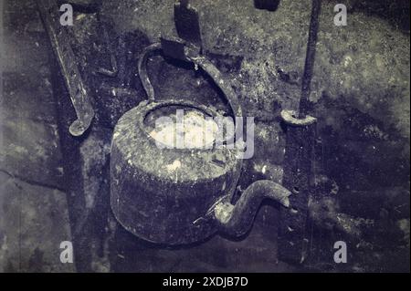 An old kettle on a hook in an old fireplace. Old photo. Stock Photo