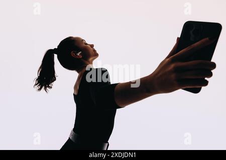 Female dancer performs dynamic dance moves with expressive body language. Listening to music on her mobile phone with earbuds in, she embodies a fit l Stock Photo