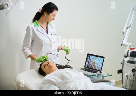 Middle-aged lady checks the condition of her hair using a trichoscope Stock Photo