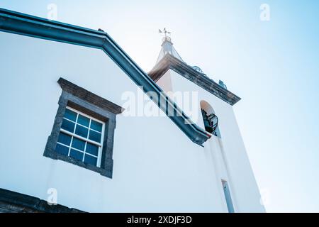 Whitewashed church facade and bell tower in Seixal, Madeira, Portugal, viewed from below against a clear blue sky. Stock Photo