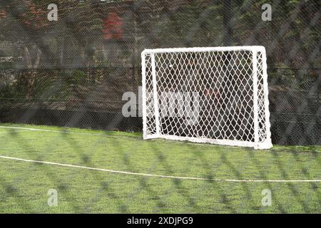 An empty soccer goal on a green artificial turf field, with a net fence in the foreground. Stock Photo
