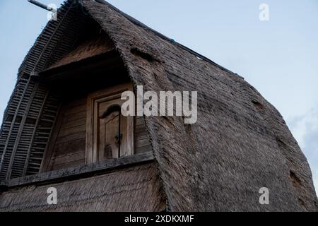 A close-up view of a traditional thatched roof house with a wooden window. The roof is made of natural materials, giving it a rustic appearance. The s Stock Photo