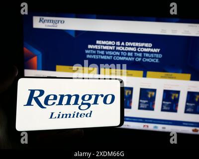 Person holding smartphone with logo of South African investment company Remgro Limited in front of website. Focus on phone display. Stock Photo