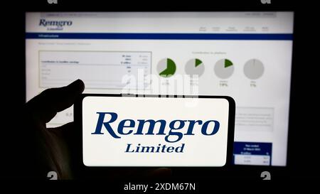 Person holding cellphone with logo of South African investment company Remgro Limited in front of business webpage. Focus on phone display. Stock Photo