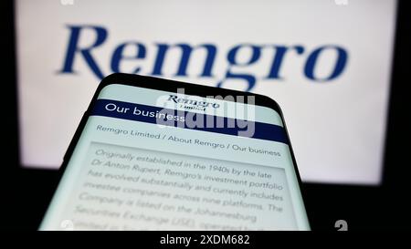 Mobile phone with website of South African investment company Remgro Limited in front of business logo. Focus on top-left of phone display. Stock Photo