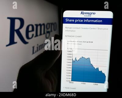 Person holding cellphone with webpage of South African investment company Remgro Limited in front of logo. Focus on center of phone display. Stock Photo