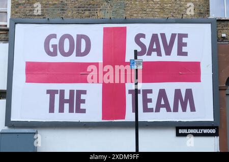 London, UK, 23rd June, 2024. A St George's flag billboard design with the words 'God Save the Team', by artist Corbin Shaw appears in a variety of different locations seeking to question what England represents today. Credit: Eleventh Hour Photography/Alamy Live News Stock Photo