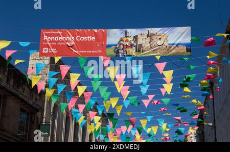 Colorful bunting flags strung across a street in Falmouth Cornwall with a clear blue sky and Pendennis castle advertisement. Stock Photo
