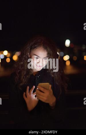 Beautiful woman standing on terrace at night, making phone call, holding smartphone, scrolling. Stock Photo