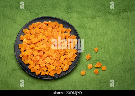 dried mango fruit diced - black ceramic palte on a green textured paper with a copy space Stock Photo