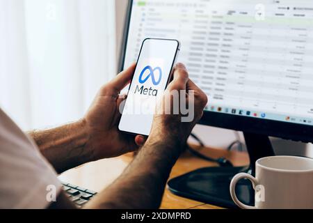 Man holding a smartphone showing the Meta logo on the mobile phone screen. Computer with Facebook Business Manager on the monitor in the background. R Stock Photo