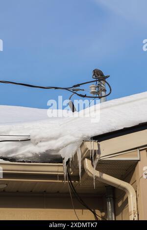 Residential power line service mast on rooftop with cables encased in ice and snow in winter. Stock Photo