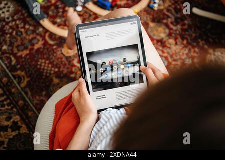 London, United Kingdom - Jun 11, 2023: A woman holding and reading an iPad displaying an announcement for Apple Vision Pro VR headset, with the headline Apps leap into life showing various app icons on the screen, set in a cozy indoor environment. Stock Photo