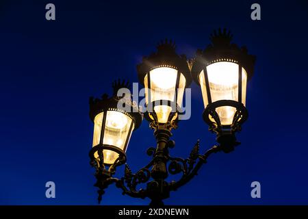 Street light with three glowing lights illuminating the night. The lamps are lit up in a way that they are all lit up at the same time, creating a sen Stock Photo