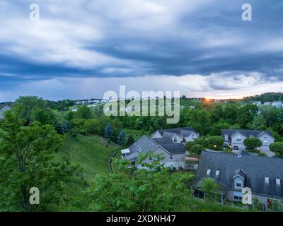 A unique glimpse of a thunderstorm over a Pennsylvania neighborhood, where dramatic clouds, a setting sun, and a striking lightning flash create a bre Stock Photo