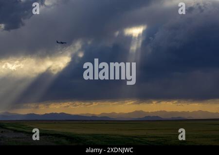 An airplane flying in the stormy sky above the Colorado prairies with the Rocky Mountains visible in the distance Stock Photo